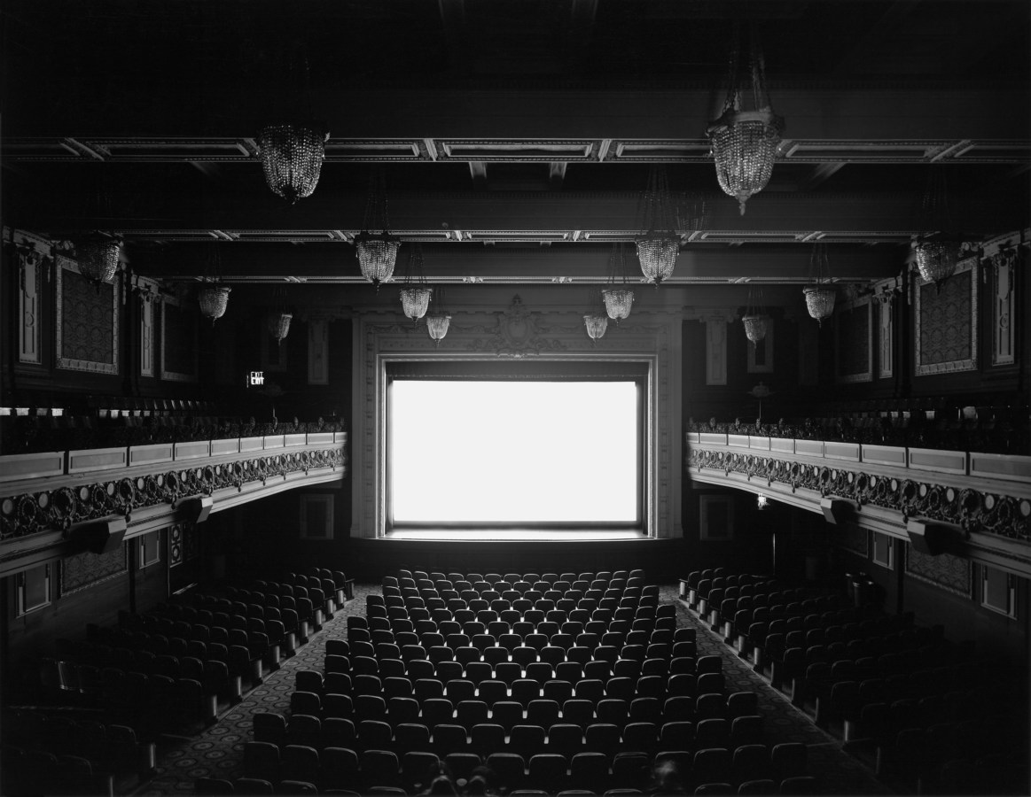 Black and white photograph of an empty theater displaying a glowing white screen