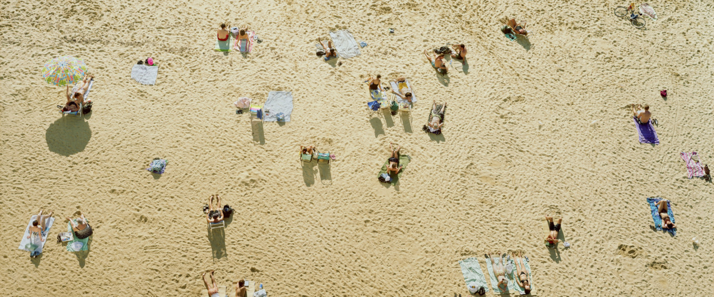 Color aerial photograph of beach-goers reclining on blankets on a sandy yellow beach