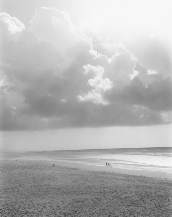 Black-and-white vertical photo of brightly lit clouds over a beach
