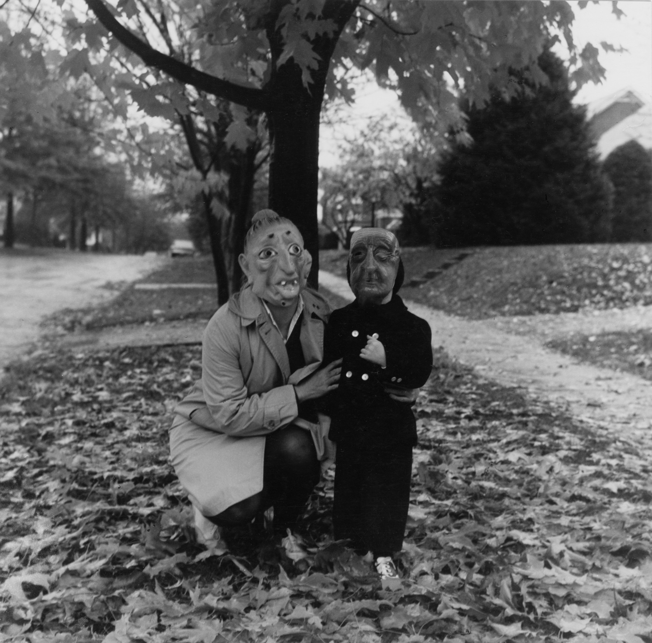 Black and white photograph of two masked figures on a leaf-covered front lawn front lawn