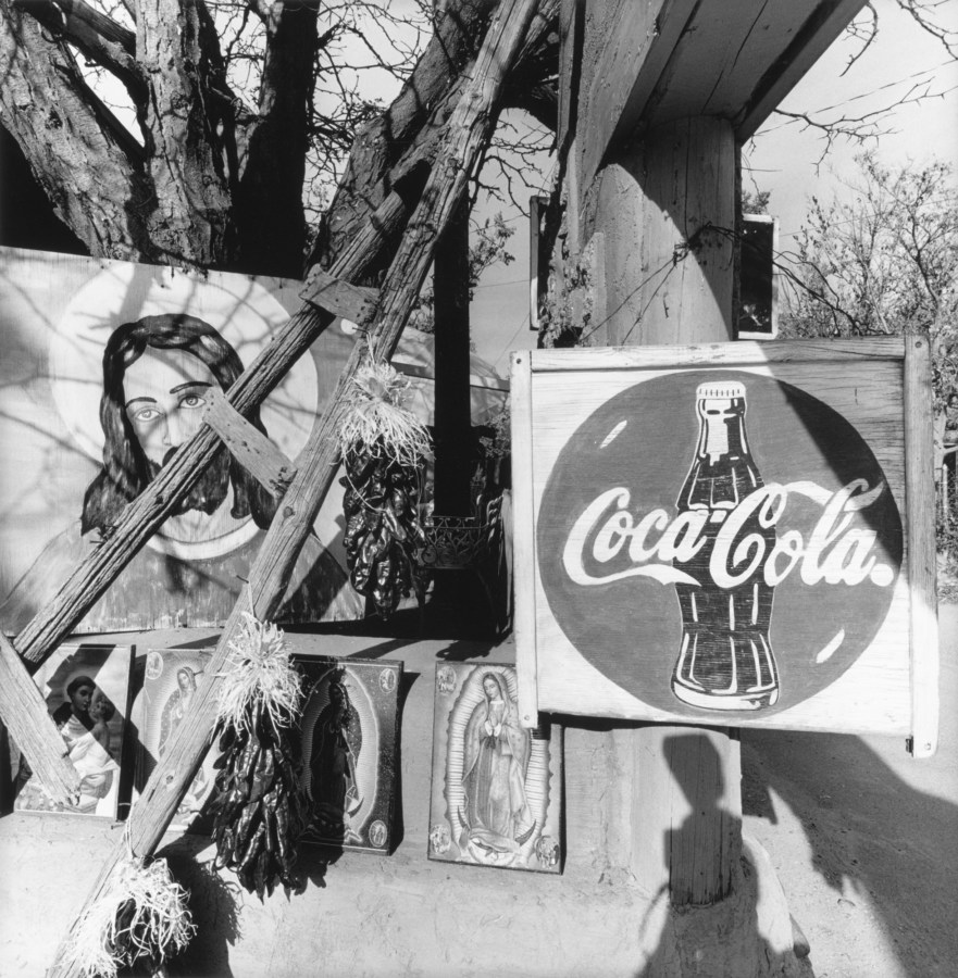 Black-and-white photograph of a Coca Cola sign and paintings of Jesus