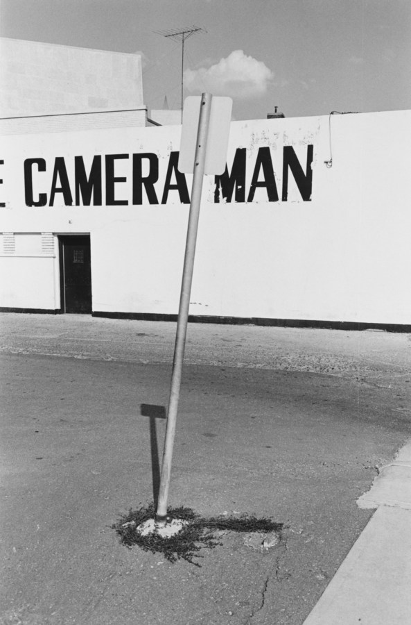 Black-and-white photograph of a street sign and a building with the text camera man painted on the side