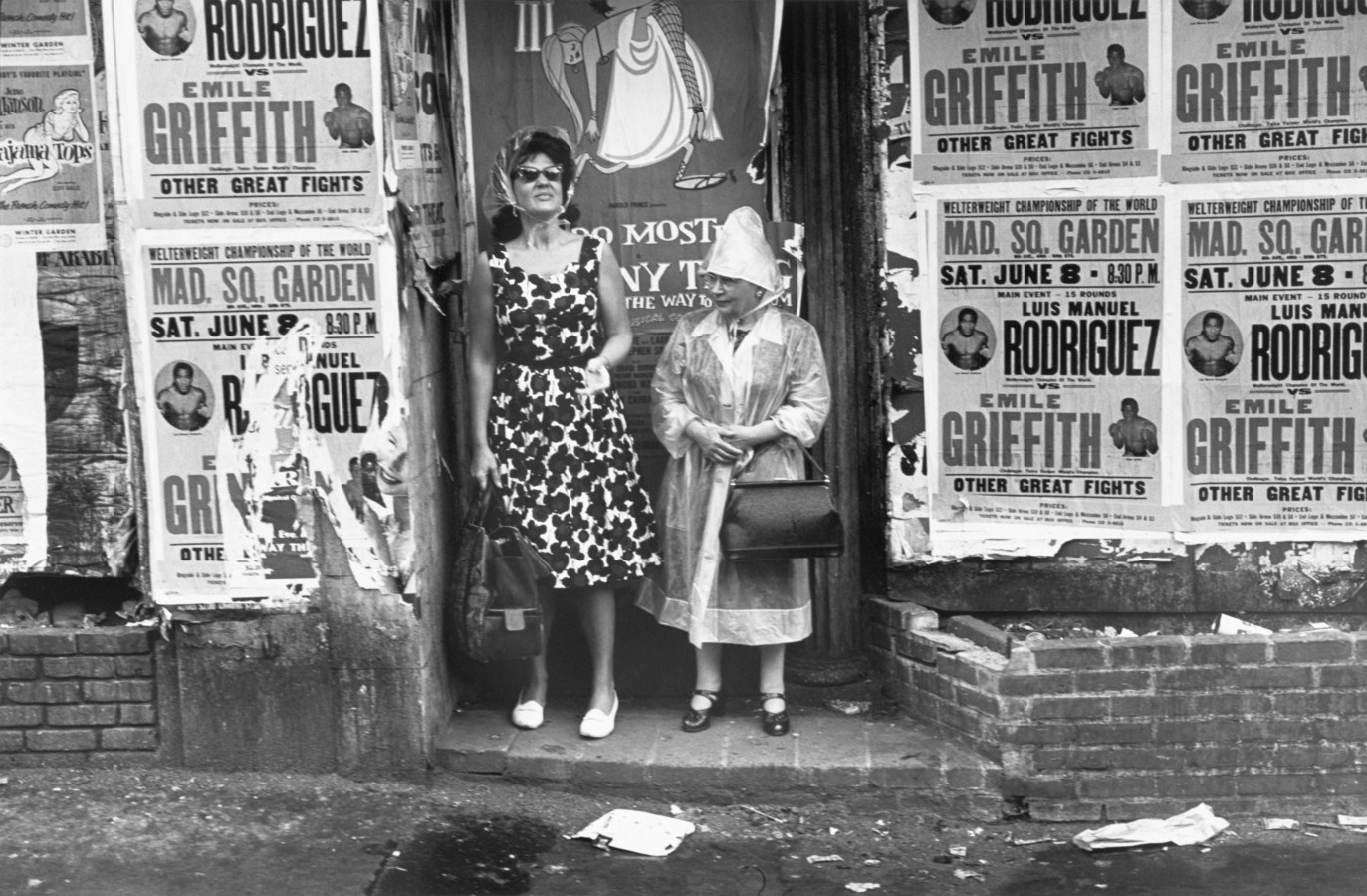 Black-and-white photograph of two women standing in a doorway of a building covered in boxing advertisements