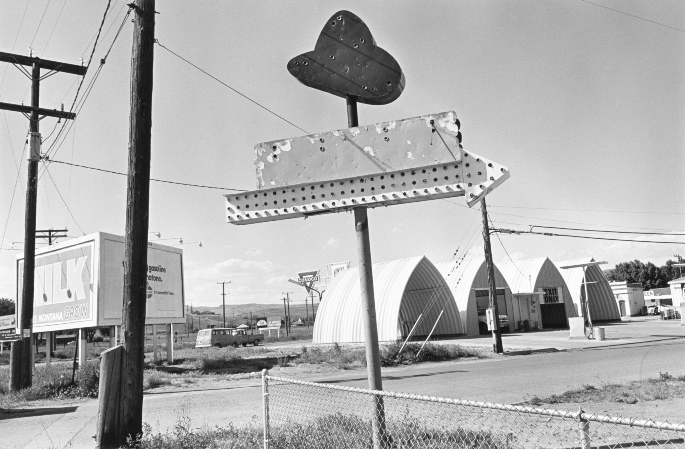 Black-and-white photograph of an old weathered neon sign shaped like a cowboy hat with an arrow pointing right