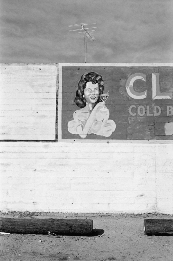 Black-and-white photograph of the side of a building with a hand painted sign of a woman holding a cocktail