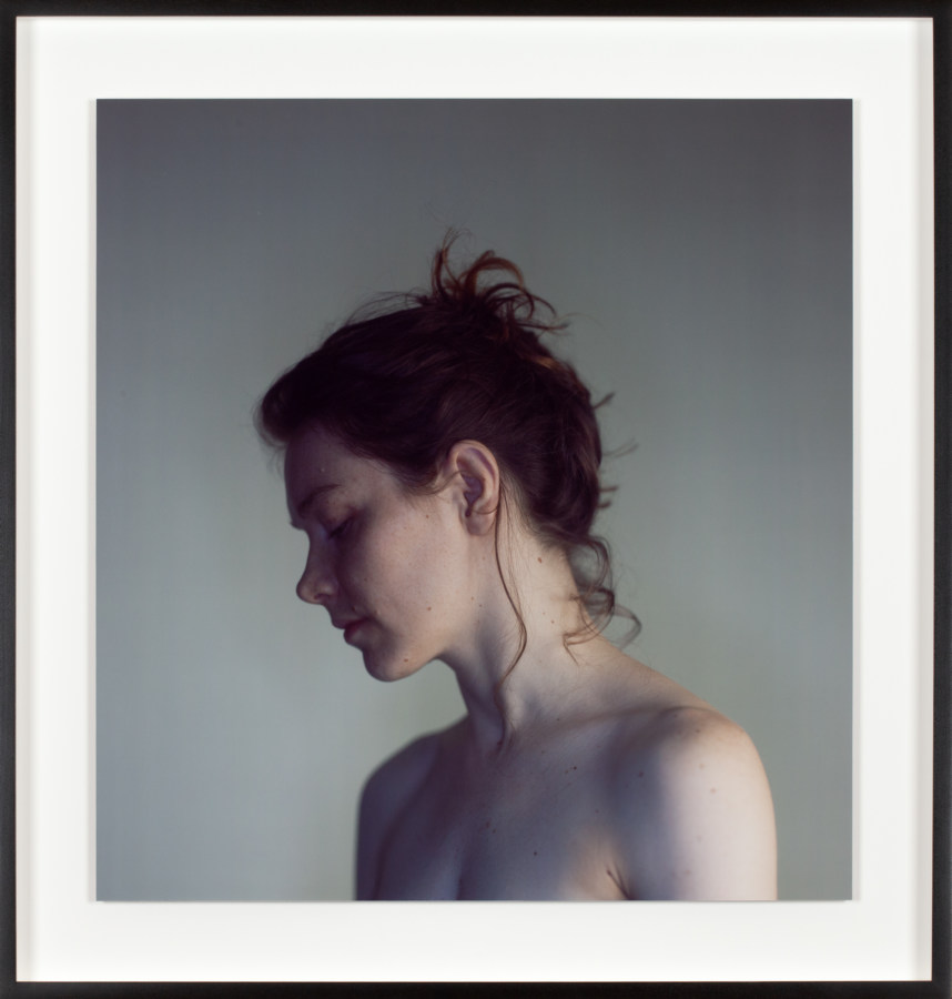 Color photographic portrait of the facial profile and shoulders of a topless young woman with her eyes closed and hair tied up