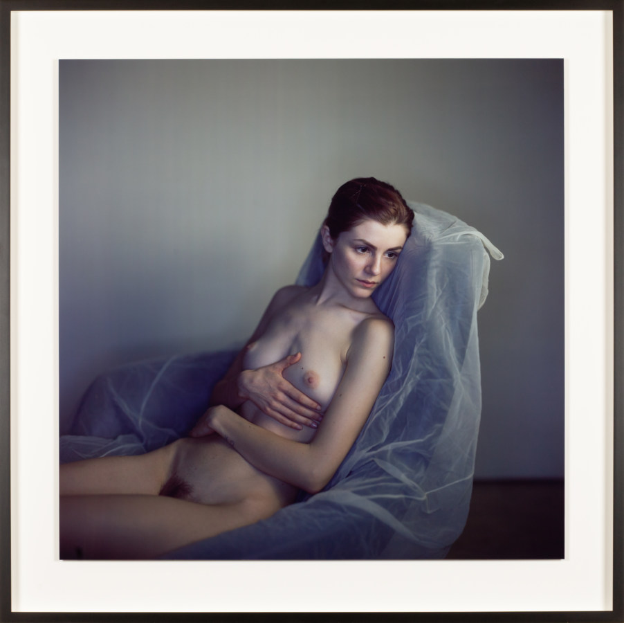 Color photographic portrait of a nude young woman reclining in a plastic-covered chair