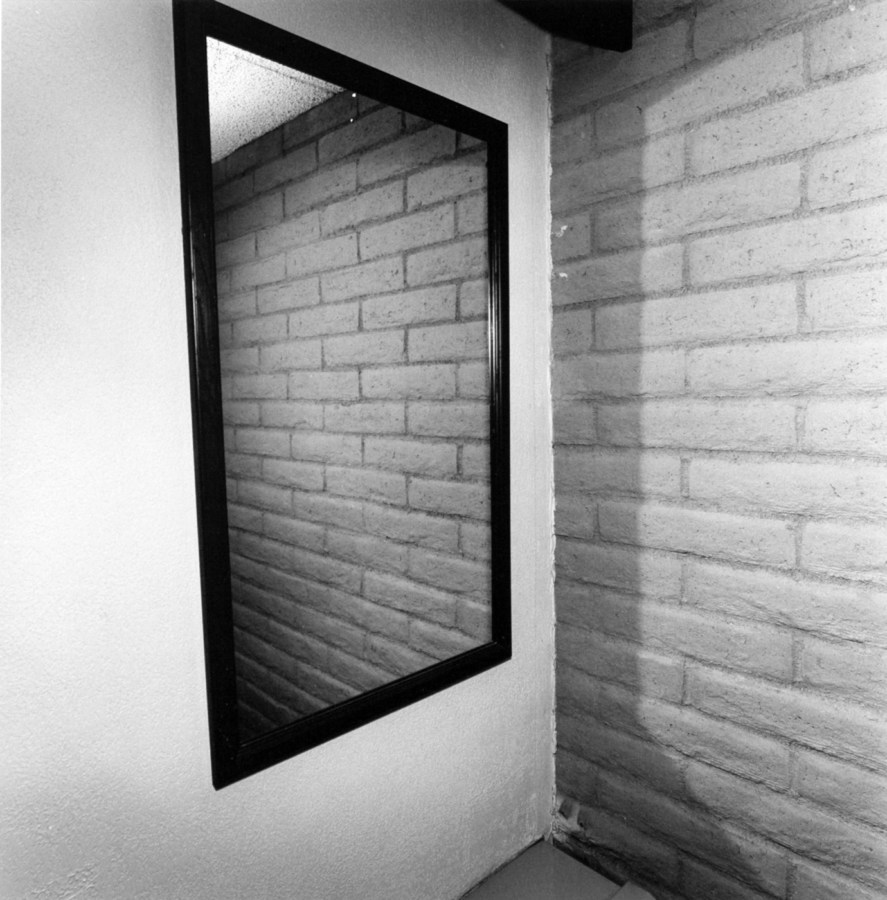 A black and white photograph of room corner with a brick wall reflected in a mirror