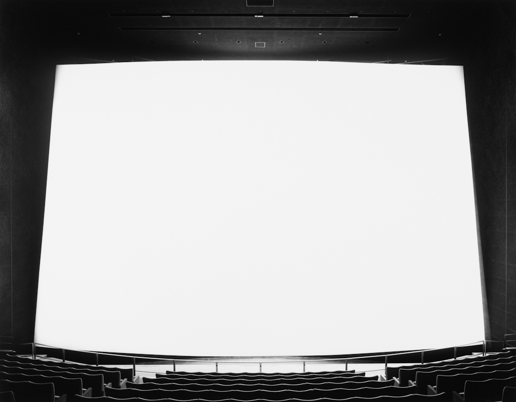 Black-and-white photograph of an empty movie theater with an extra large glowing white screen