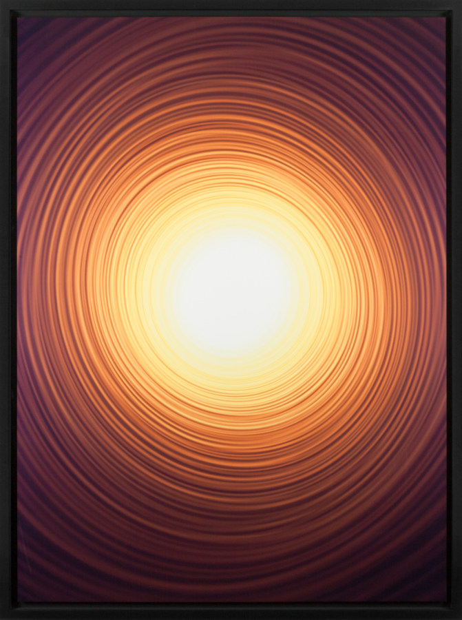 Color photograph of a bright yellow-white circle emanating fading orange rings of light on a black background
