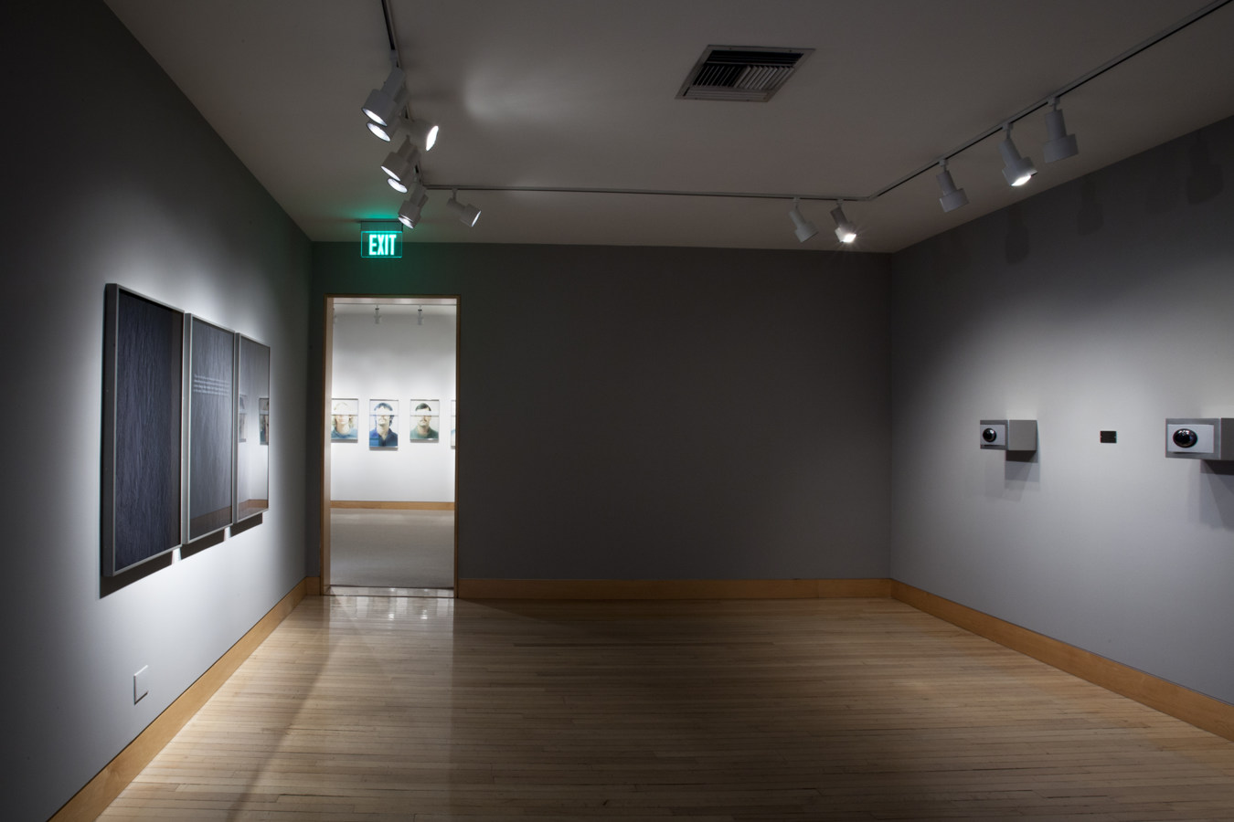 Color image of both framed and sculptural works on grey gallery walls