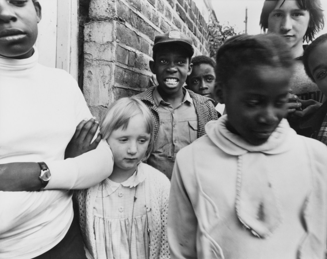 Black-and-white photograph of a group of children gathered near a brick wall