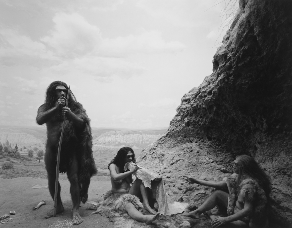 Black-and-white photograph of a museum diorama of early humans working with animal skins