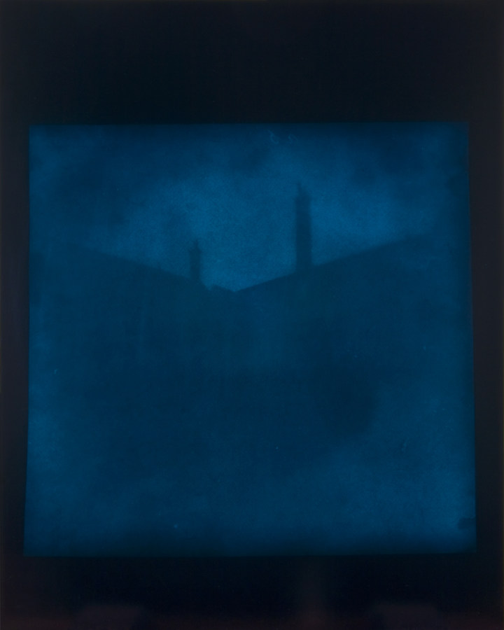 Dark blue-toned photograph of a v-shaped roofline with two protruding narrow chimneys