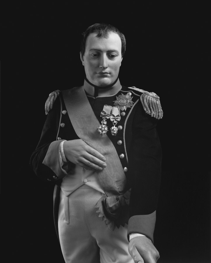 Black-and-white frontal portrait of a wax figure of a man in nineteenth century jacket with shoulder tassels, medals and a sash