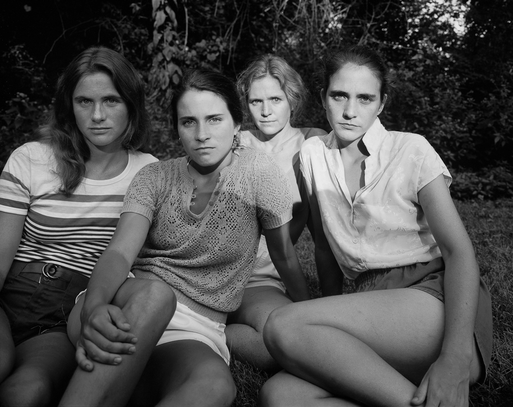 Black-and-white photographic portrait of four young women seated outdoors on grass