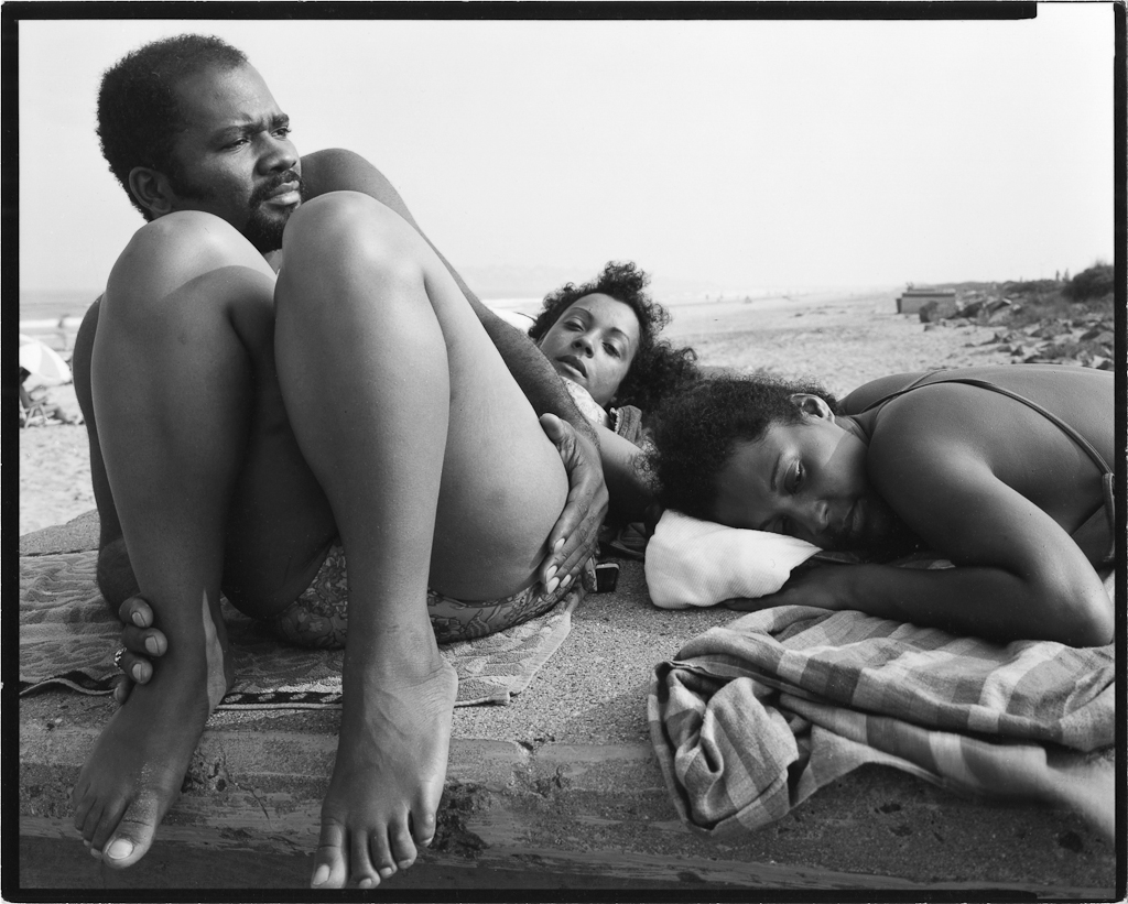 Black-and-white photograph of three young adults reclining on blankets on a beach