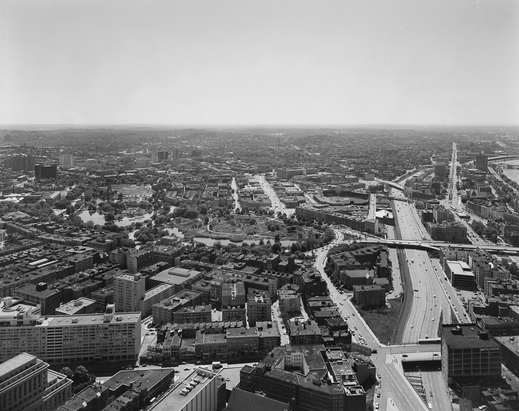 Black-and-white photograph of a highway and surrounding neighborhoods at midday under a clear sky
