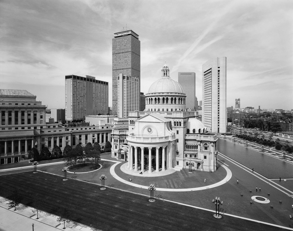 Black-and-white photograph of a Greco-Roman style building with a domed roof amid modern city high rise buildings