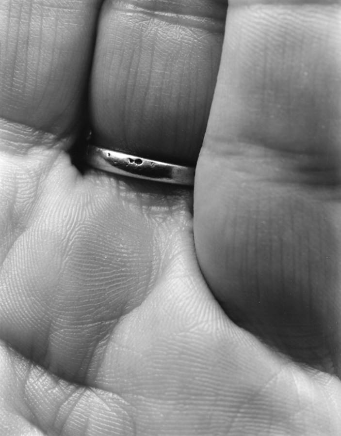 Black-and-white close-up photograph of of the inner base of three fingers, one wearing a ring