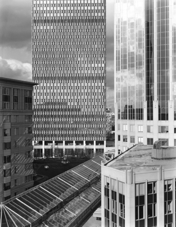 Black-and-white photograph of glass-fronted high-rise buildings under a cloudy sky