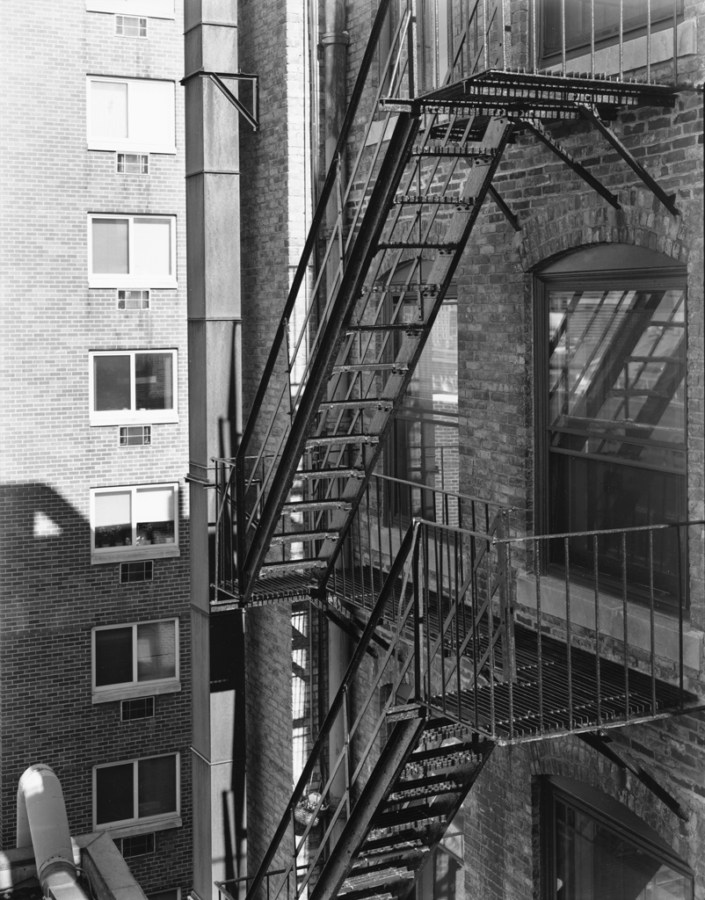 Black-and-white photograph of fire escapes on the shadowed side of a brick building