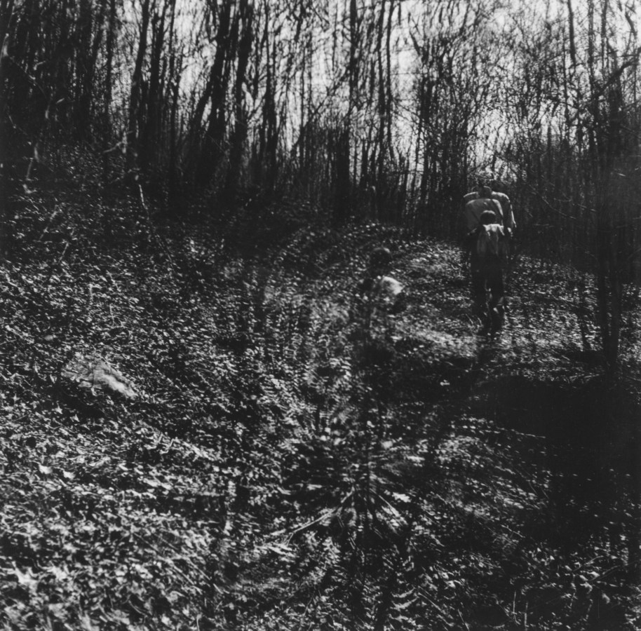 Black-and-white multiple-exposure photograph of two figures standing amid bare trees