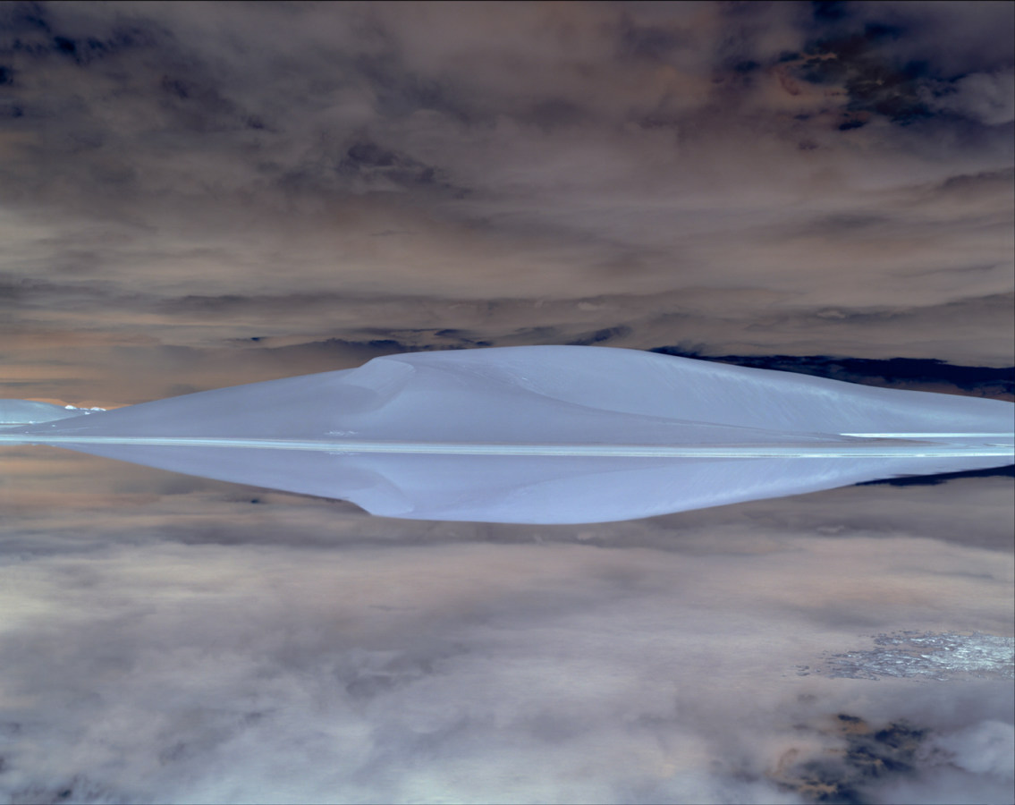 Inverted color photograph of a sand dune reflected in a still body of water