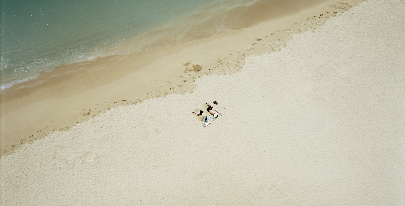 Color aerial photograph of two people curled up on a sandy beach near the waterline