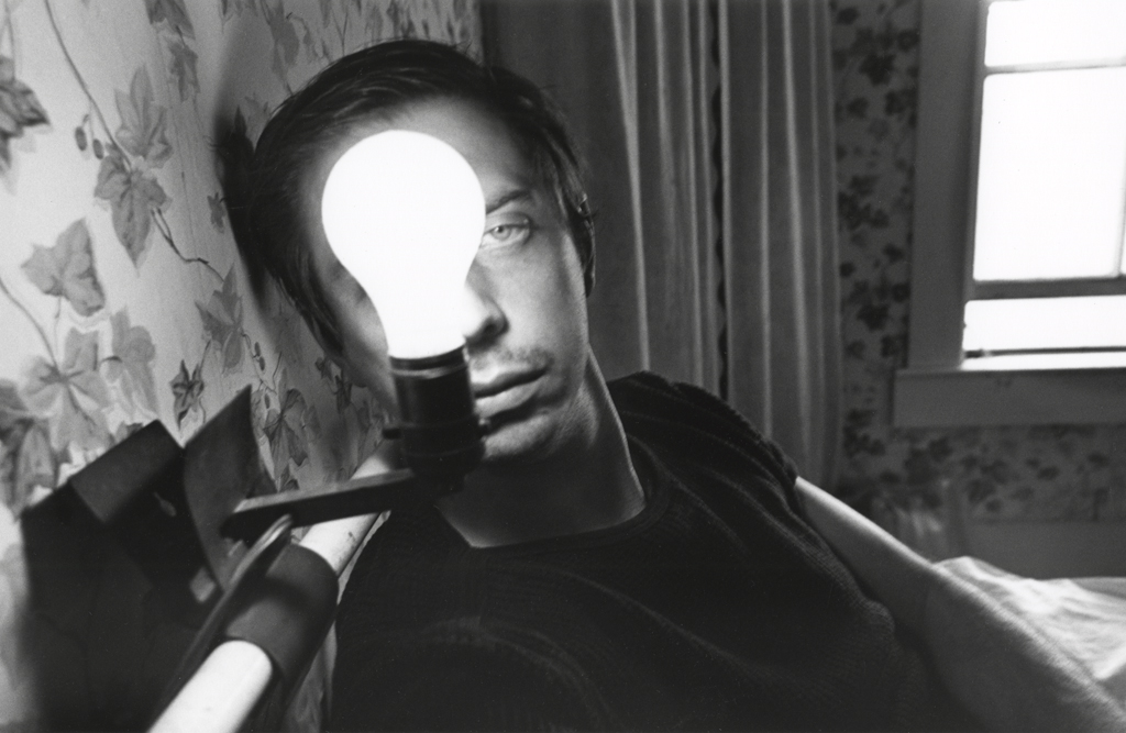 A black and white photograph of a self portrait of the artist with an illuminated lightbulb in front of his face