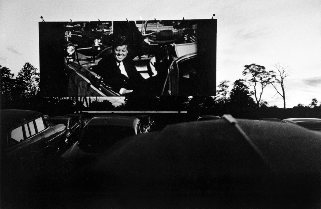 Black-and-white photograph of JFK on screen at a drive in theater