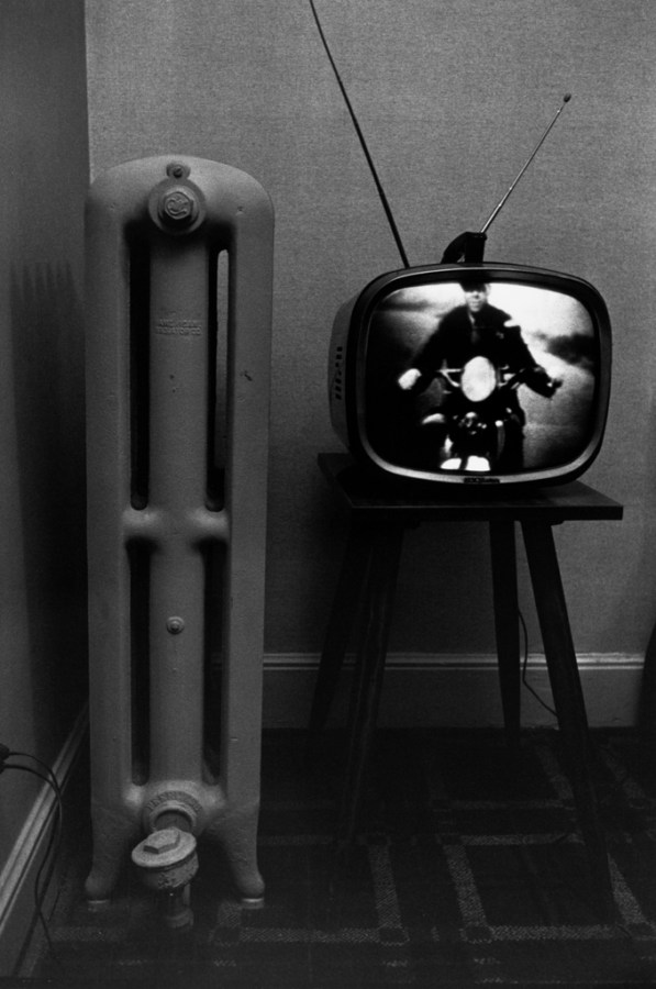 Black-and-white photograph of a television with a motorcyclist on screen and a radiator
