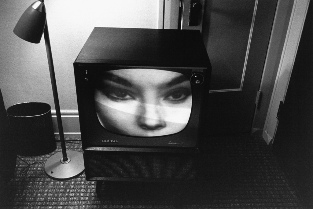 Black-and-white photograph of a television with an up close image of a womans face on screen