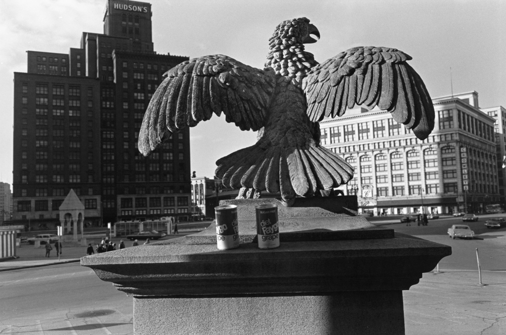 Black and white photograph of an eagle monument with buildings in the background