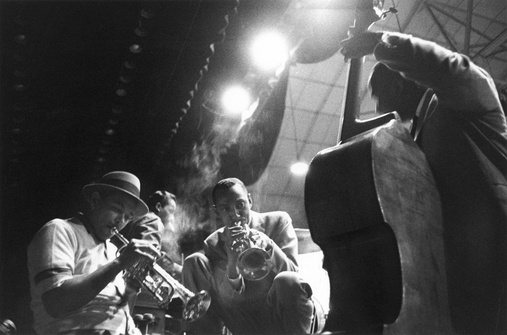 Black and white photograph of three men playing instruments in a smoky room