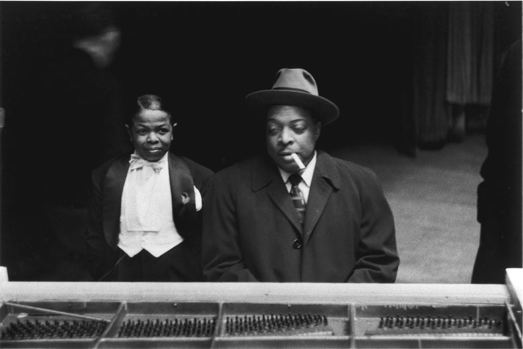 Black and white photograph of a man smoking a cigar and a boy at a piano
