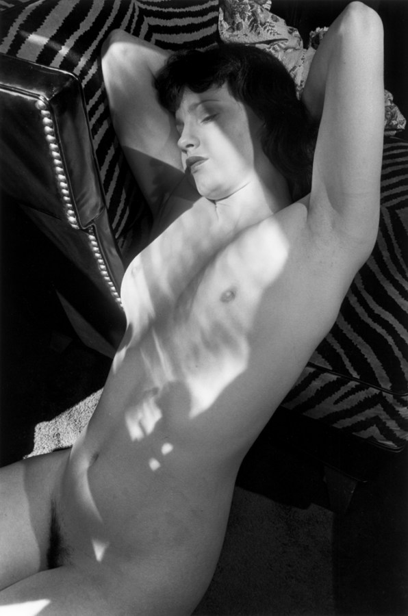 A black and white photograph of a nude woman laying in a beam of light