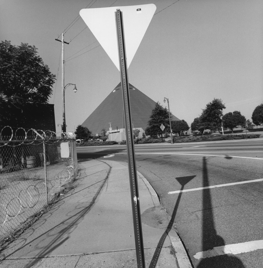 A black and white photograph of the back of a yield sign lined up with a pyramid in the distance