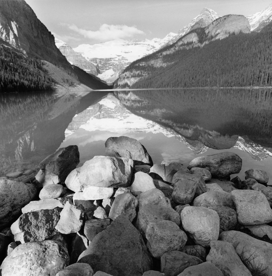 Black-and-white photograph of mountains and a lake and rocks in the foreground