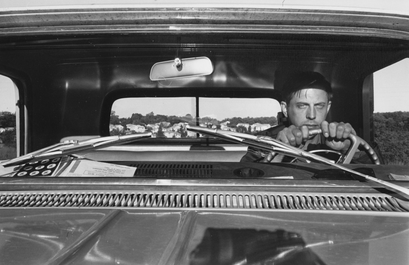 A black and white photograph of a self portrait of the artist at the wheel of a pickup truck