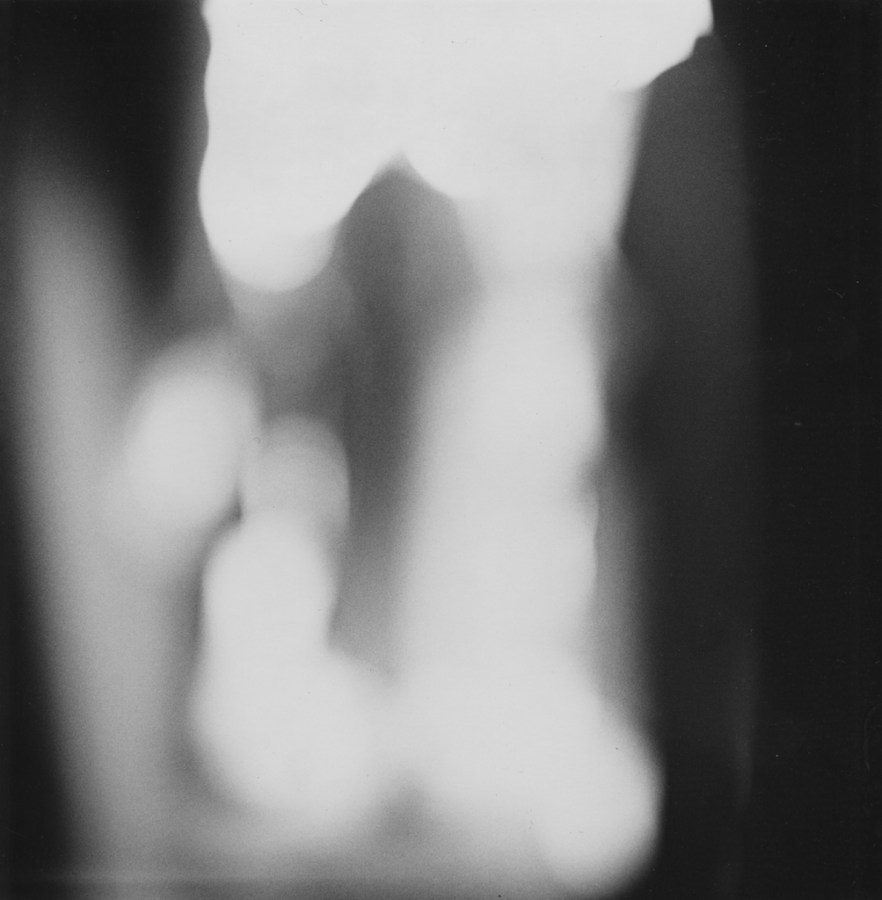 Black-and-white out-of-focus photograph of a figure standing between two dark blobs