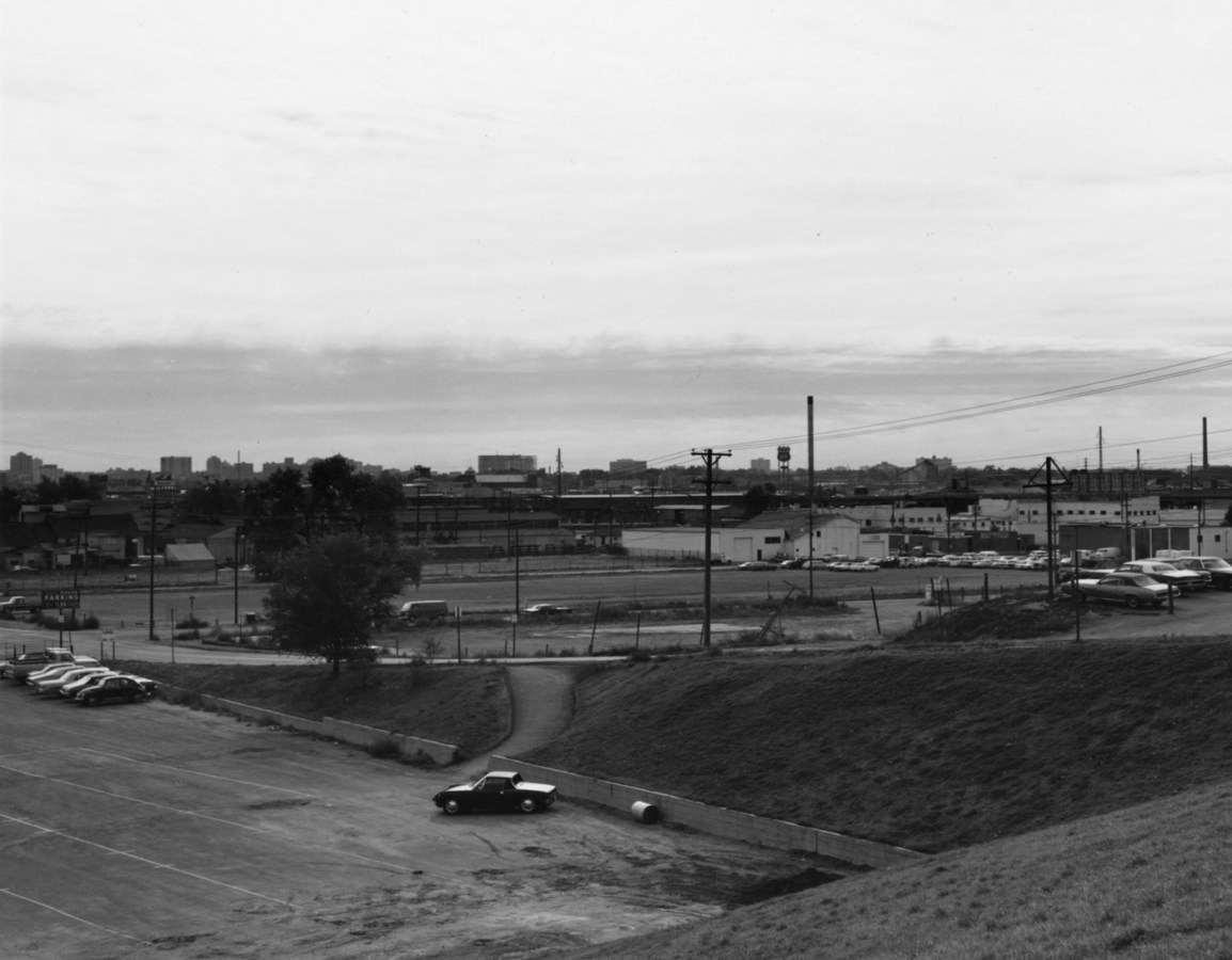 A black and white photograph of an industrial area with parking lots and cars.