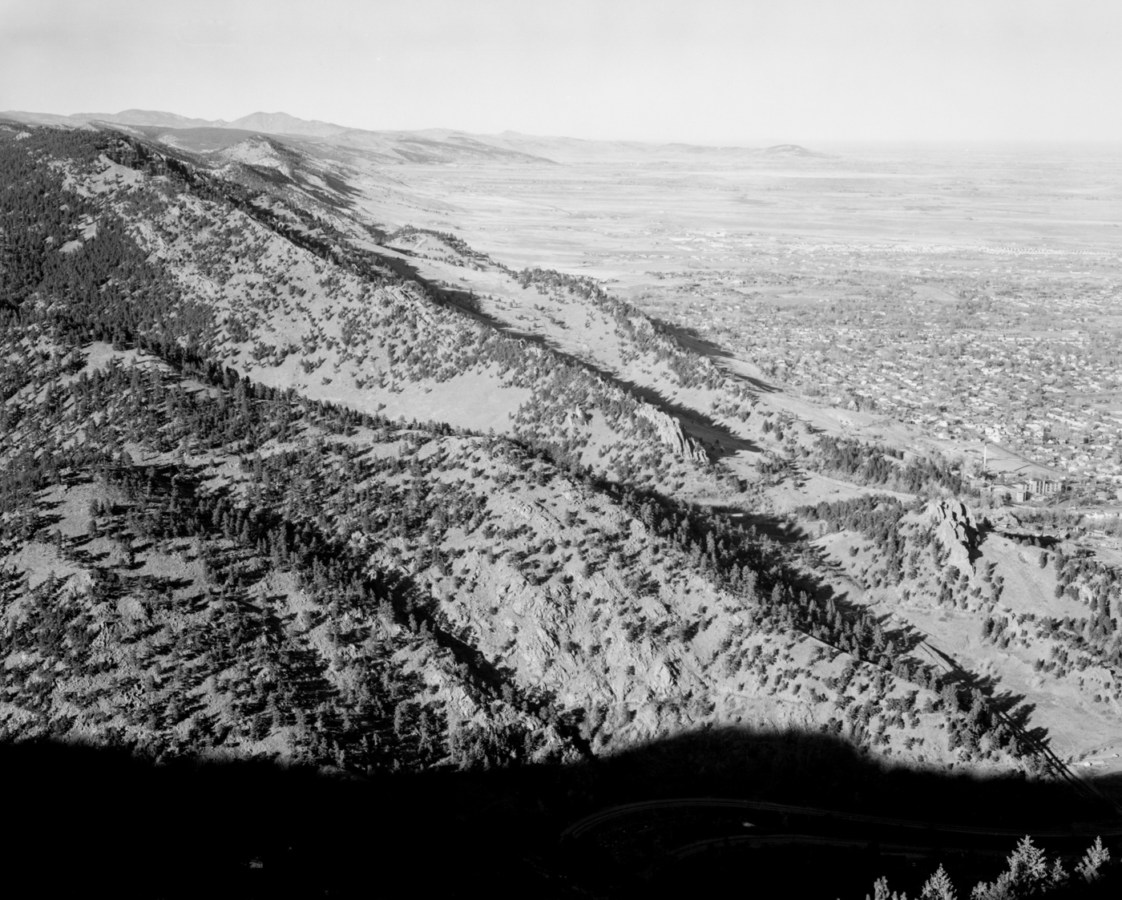 A black and white photograph of expansive mountains with trees and a hazy horizon.
