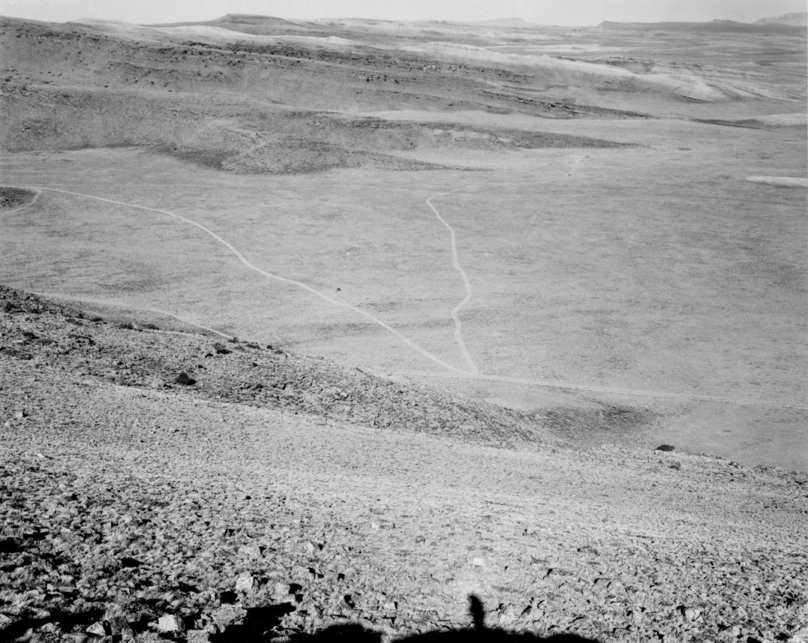 A black and white photograph of an expansive valley with roads running through it with mountains on the horizon.
