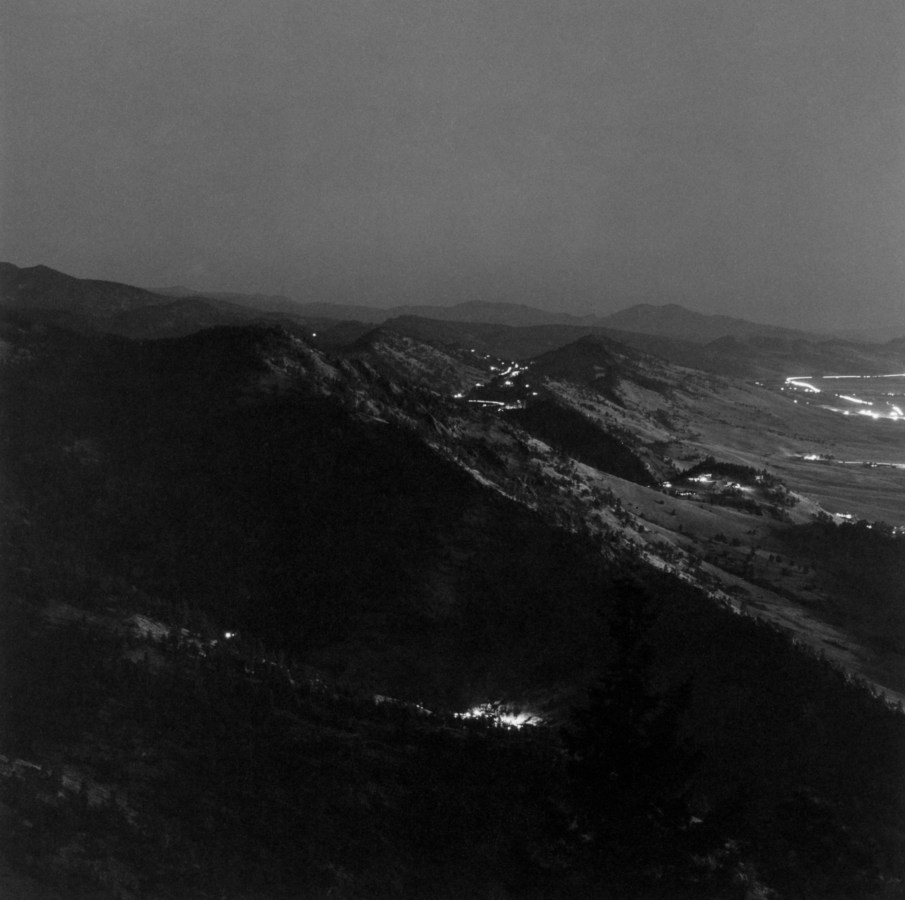 Black-and-white photograph of distant town lights and mountains at night