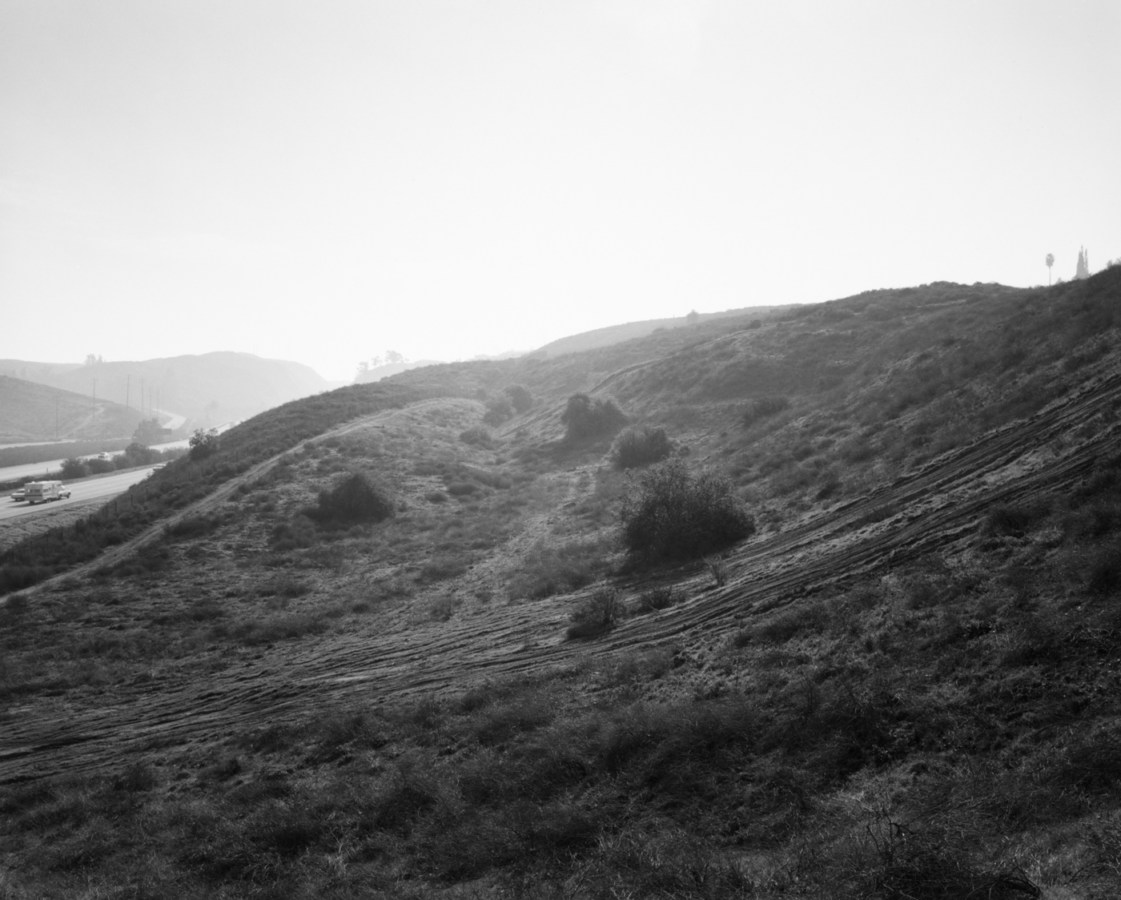 Black-and-white photograph of light streaming over a hillside with a freeway to the left