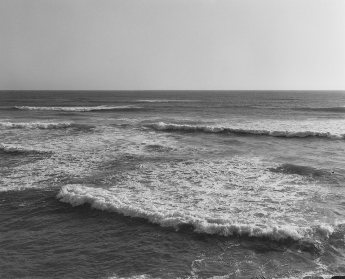 Black-and-white photograph of a seashore with small waves and a clear sky