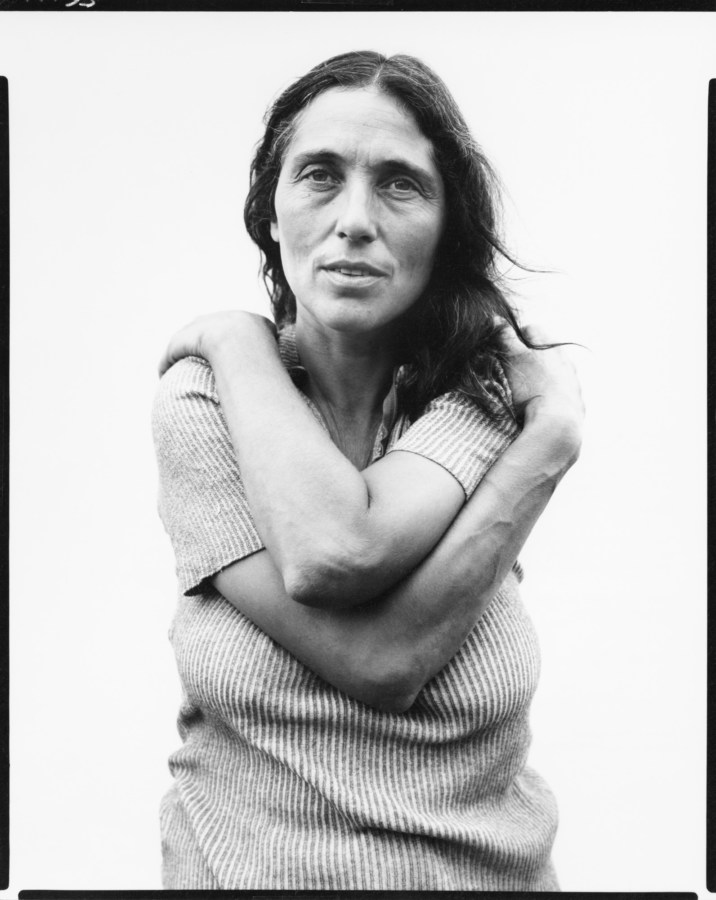 black-and-white photograph of a woman with her arms wrapped around herself against a white background