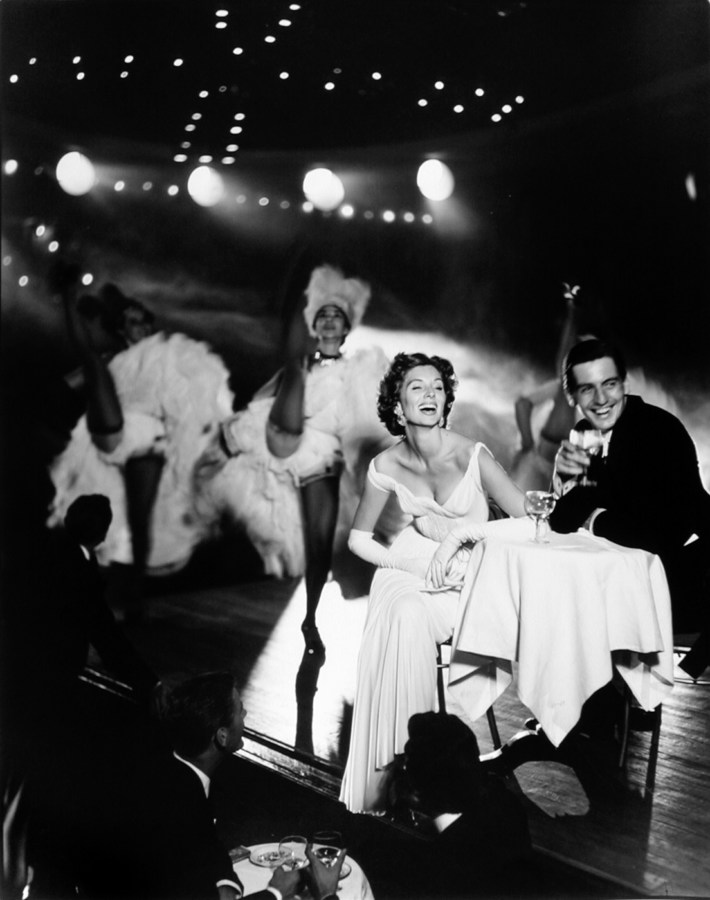 black-and-white photograph of a man and woman at a table on stage with dancers in the background