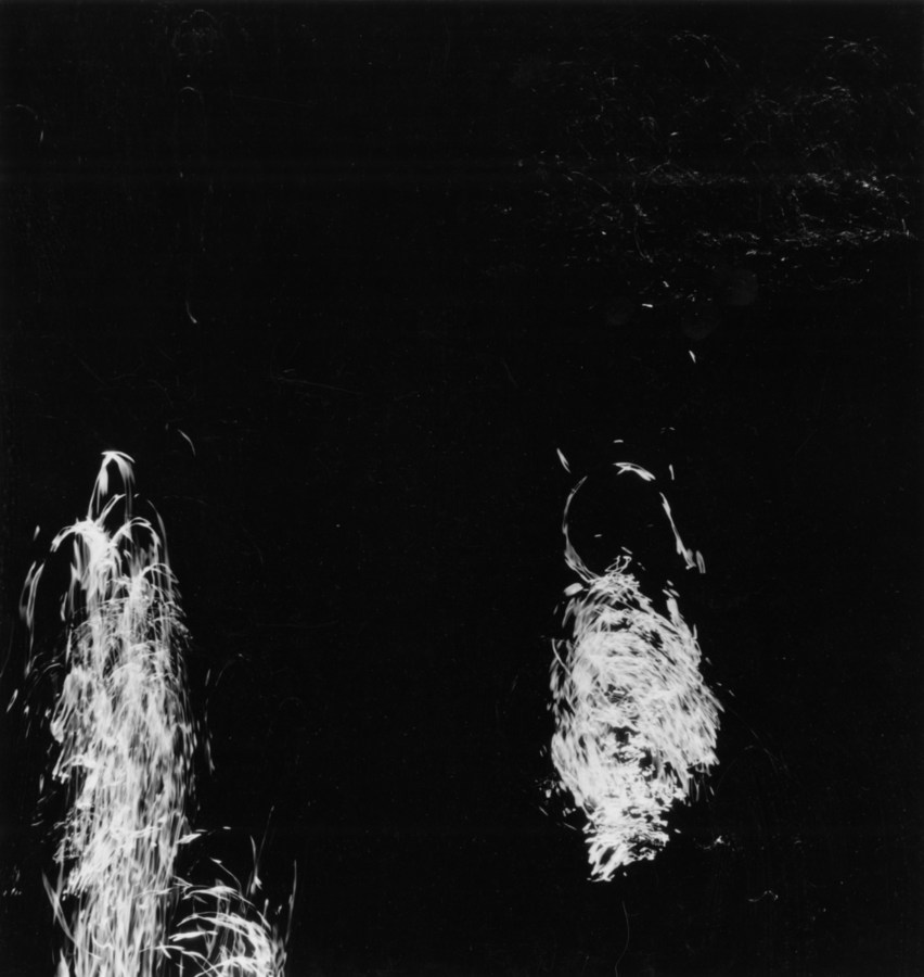 Square black-and-white long-exposure photograph of two trails of light reflecting off of moving water
